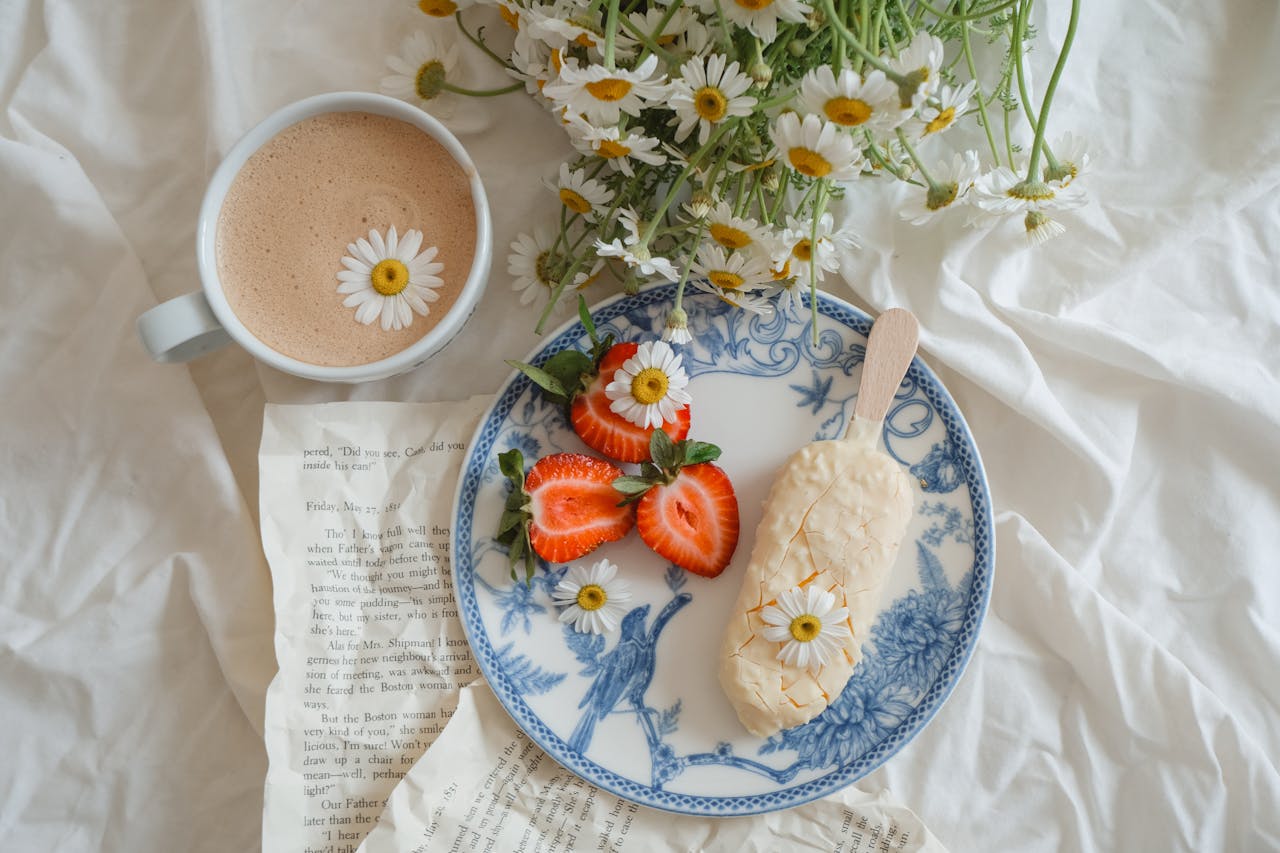 Elegant flat lay of coffee, dessert, strawberries, and flowers on blue china plate.